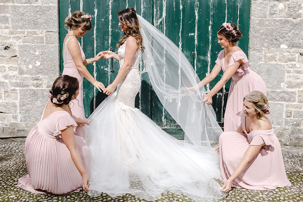 Bridesmaids getting the wedding dress just right for a bride on the morning of her wedding in South Wales